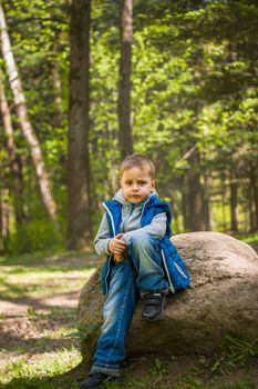 Portrait of a boy in a blue tank top in the woods in spring. Take a walk in the green park in the fresh air. The magical light from the sun's rays falls behind the boy. Spring