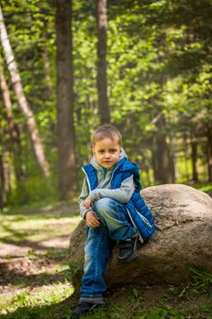 Portrait of a boy in a blue tank top in the woods in spring. Take a walk in the green park in the fresh air. The magical light from the sun's rays falls behind the boy. Spring