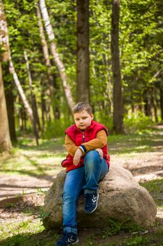 Portrait of a young man in a red tank top in the forest in spring. Walk through the green park in the fresh air. The magical light from the sun's rays falls behind the boy. Spring