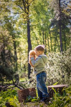 A cute boy is playing with a bear cub in the forest. The sun's rays envelop the space of the clearing with a stump. A magical story of interactions for the book. Space for copying. Selective focus.