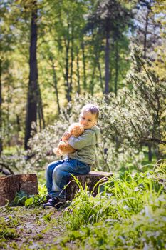 A cute boy is playing with a bear cub in the forest. The sun's rays envelop the space of the clearing with a stump. A magical story of interactions for the book. Space for copying. Selective focus.