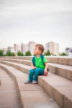 A boy is playing with a toy, sitting on the steps in the open air against the backdrop of skyscrapers and high-rise buildings. Journey. Lifestyle in the city. Center, streets.