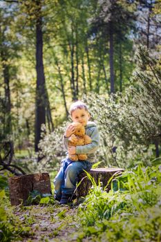A cute boy is playing with a bear cub in the forest. The sun's rays envelop the space of the clearing with a stump. A magical story of interactions for the book. Space for copying. Selective focus.