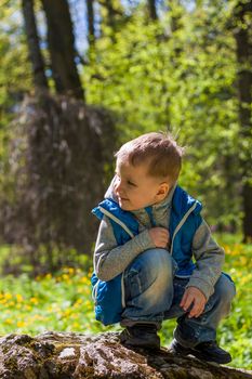 Portrait of a boy in a blue tank top in the woods in spring. Take a walk in the green park in the fresh air. The magical light from the sun's rays falls behind the boy. Spring