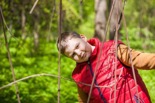 Portrait of a young man in a red tank top in the forest in spring. Walk through the green park in the fresh air. The magical light from the sun's rays falls behind the boy. Spring