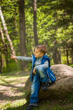 Portrait of a boy in a blue tank top in the woods in spring. Take a walk in the green park in the fresh air. The magical light from the sun's rays falls behind the boy. Spring