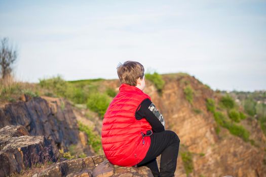 A child sits on top of a cliff and watches what is happening below. panoramic view from the top of a rocky mountain. Russia, Rostov region, skelevataya skala, the 7th wonder of the Don world. Landscape