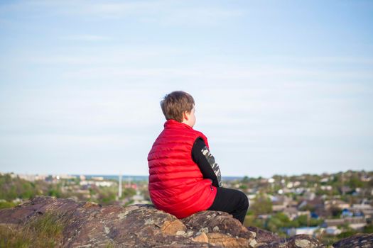 A child sits on top of a cliff and watches what is happening below. panoramic view from the top of a rocky mountain. Russia, Rostov region, skelevataya skala, the 7th wonder of the Don world. Landscape