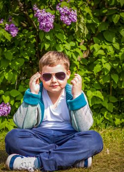 A boy poses near a lush lilac. Portrait of children with an interesting facial expression. Interactions. Selective focus. Spring