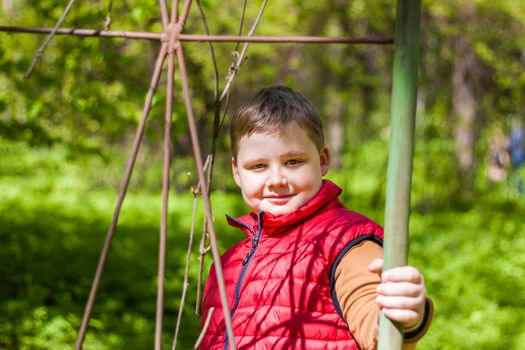 Portrait of a young man in a red tank top in the forest in spring. Walk through the green park in the fresh air. The magical light from the sun's rays falls behind the boy. Spring