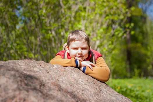 Portrait of a young man in a red tank top in the forest in spring. Walk through the green park in the fresh air. The magical light from the sun's rays falls behind the boy. Spring