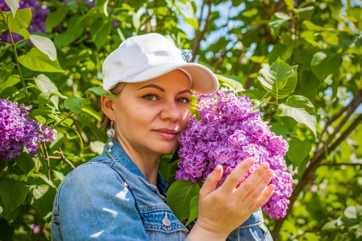 A young woman in a white cap poses near a lilac bush. Portrait of a girl. Interactions. Selective focus. Spring