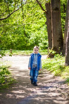 Portrait of a boy in the forest in spring. Take a walk in the green park in the fresh air. The magical light from the sun's rays is left behind. Space for copying. Selective focus. Spring