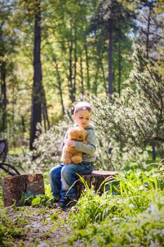 A cute boy is playing with a bear cub in the forest. The sun's rays envelop the space of the clearing with a stump. A magical story of interactions for the book. Space for copying. Selective focus.