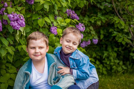 A boy poses near a lush lilac. Portrait of children with an interesting facial expression. Interactions. Selective focus. Spring