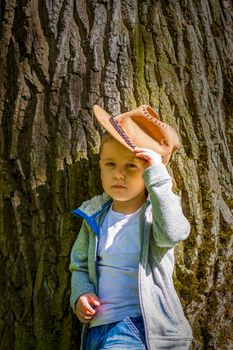 Cute boy posing in a cowboy hat in the woods by a tree. The sun's rays envelop the space. Interaction history for the book. Space for copying. Selective focus.