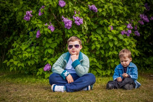 A boy poses near a lush lilac. Portrait of children with an interesting facial expression. Interactions. Selective focus. Spring