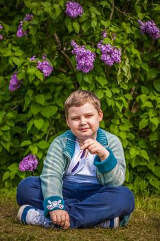 A boy poses near a lush lilac. Portrait of children with an interesting facial expression. Interactions. Selective focus. Spring