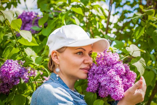 A young woman in a white cap poses near a lilac bush. Portrait of a girl. Interactions. Selective focus. Spring