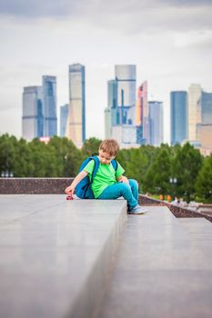 A boy is playing with a toy, sitting on the steps in the open air against the backdrop of skyscrapers and high-rise buildings. Journey. Lifestyle in the city. Center, streets.