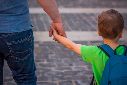 A father holds his son's hand while walking down a city street.  Travel. Lifestyle in the city. Center, streets. Summer, a walk.