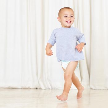 Full length shot of a cute little boy walking around the house in a nappy and t-shirt.