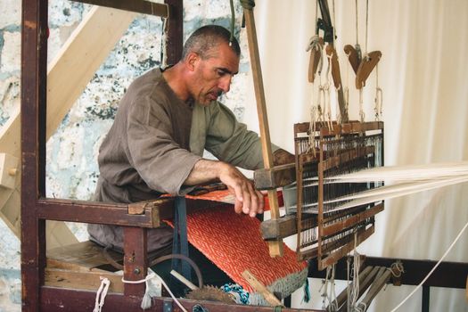MDINA / MALTA - MAY 04 2019: Man using a foot-treadle floor loom to weave cloth