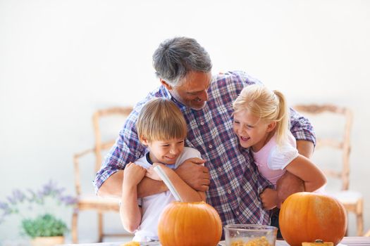 A father embracing his son and daughter while hollowing out pumpkins for halloween.