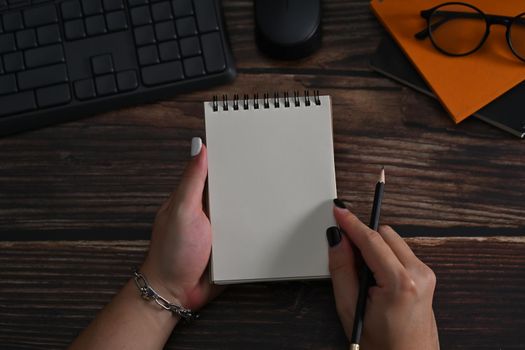 Close up view woman hand holding pencil and empty notebook.