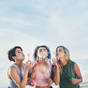 Cropped shot of three friends blowing bubbles at the beach.