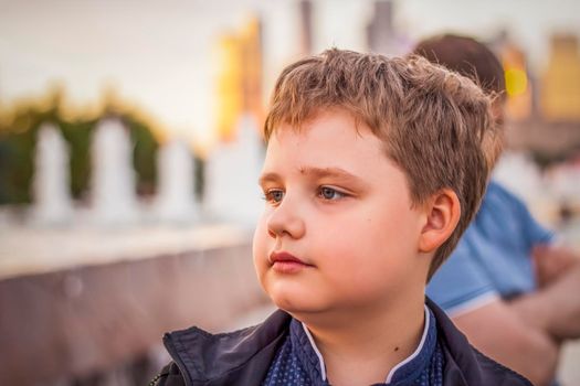 Portrait of a child, a boy against the backdrop of urban landscapes of skyscrapers and high-rise buildings in the open air. Children, Travel. Lifestyle in the city. Center, streets. Summer, a walk.