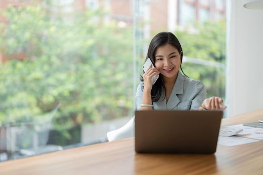 Portrait young accountant hand holding smartphone to call marketing consultants and using laptop computer to analyze sales growth in the global workplace market. accounting concept.