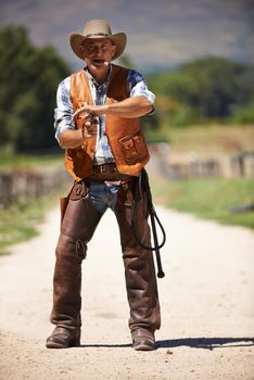 A mature cowboy outdoors with his gun drawn.