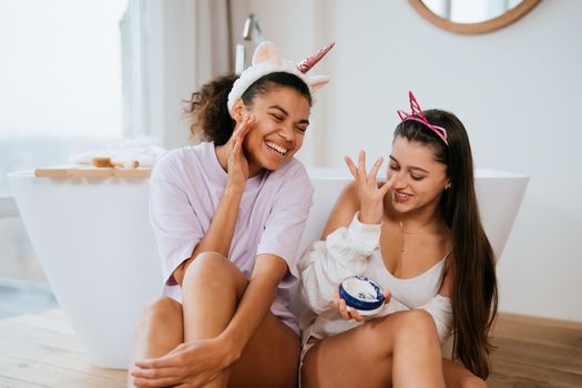 Two girls in the bath playing with face cream. Close view