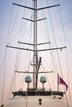 Mast of a luxury sailing yacht with sails down showing the rigging against a multi-colored sky