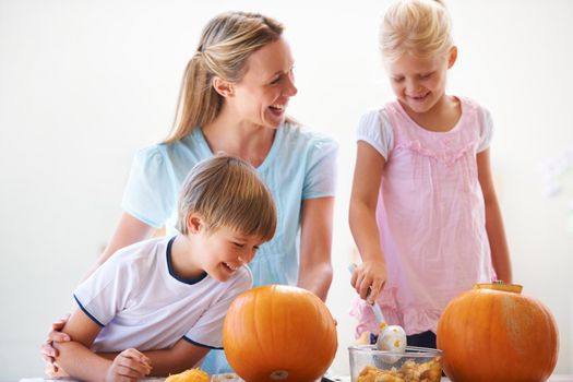 A mother, her son and her daughter hollowing out pumpkins for halloween.