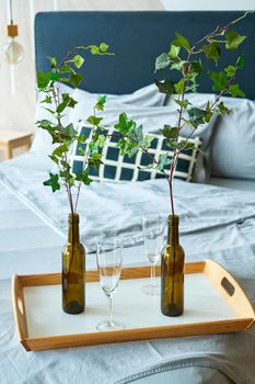 stylish interior of sleeping room with double bed and branches in vine bottles on the tray.