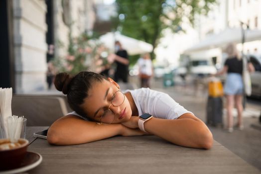 Bored, indifferent girl at a table in a street cafe with a Cup of coffee
