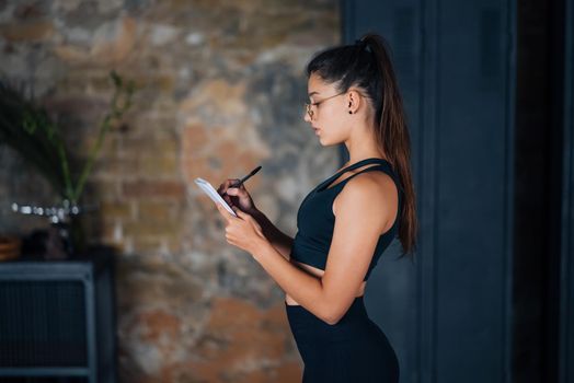 Cute women standing writing down something into the notebook.