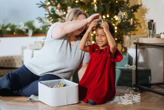 Parent and little child having fun near Christmas tree indoors. Loving family with presents in room.