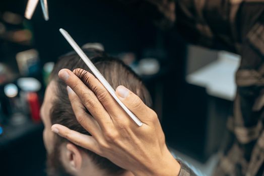 Great time at barbershop. Cheerful young bearded man getting haircut by hairdresser while sitting in chair at barbershop