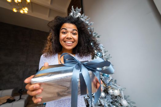 Woman gives a gift to his friend in the camera. Portrait of a young woman of Afro appearance ethnic, black curly hair brunette.
