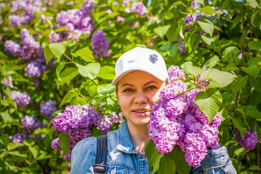 A young woman in a white cap poses near a lilac bush. Portrait of a girl. Interactions. Selective focus. Spring