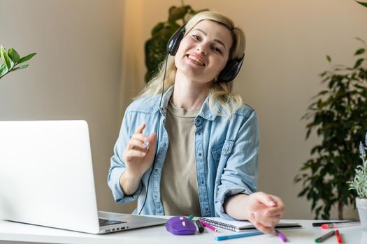 Image of young pleased happy cheerful cute beautiful business woman sit indoors in office using laptop computer listening music with earphones.