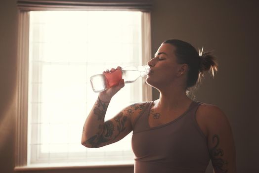 Shot of a young woman drinking water after her workout at home.