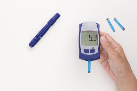 Top view of cropped woman hand holding glucometer with nine point three 9.3 mmol per liter glycemic index on display with blooded test strip inside, lancet and test strips on white background
