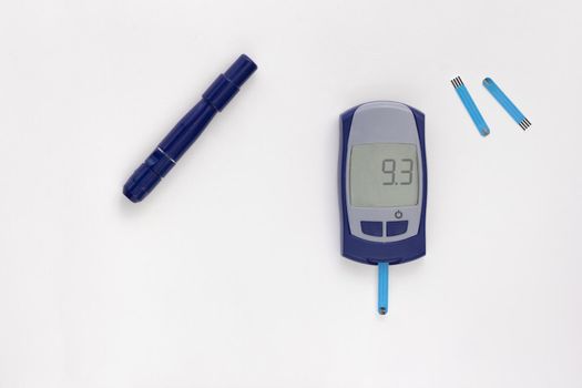 Top view of glucometer with nine point three 9.3 mmol per liter glycemic index on display with blooded test strip inside, lancet and test strips on white background