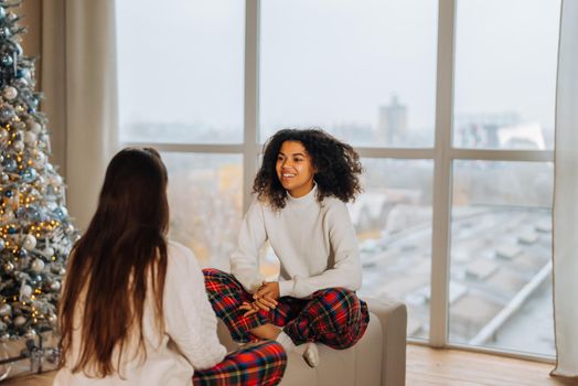 Two female student friends sitting on the couch at home. Multiethnic women.