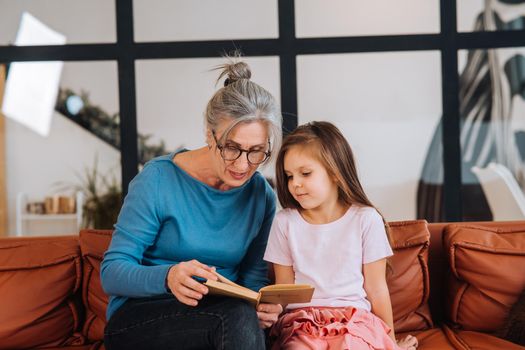 Nice elderly woman grandmother reading story to granddaughter. Happy family at home concept