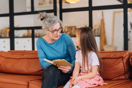 Nice elderly woman grandmother reading story to granddaughter. Happy family at home concept